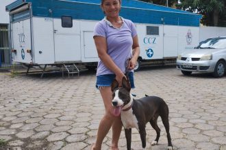 Mulher sorrindo com cachorro em frente a trailer CCZ, o Castramóvel da Prefeitura de Manaus