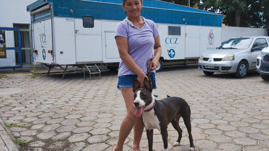 Mulher sorrindo com cachorro em frente a trailer CCZ, o Castramóvel da Prefeitura de Manaus