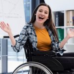 Mulher sorrindo e gesticulando em cadeira de rodas em um escritório.