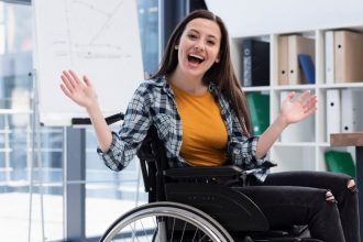Mulher sorrindo e gesticulando em cadeira de rodas em um escritório.
