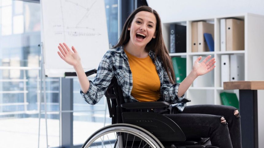 Mulher sorrindo e gesticulando em cadeira de rodas em um escritório.