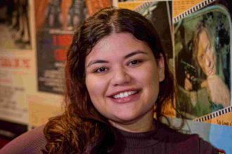 Mulher sorrindo em frente a cartazes de filmes, possivelmente em um cineclube.