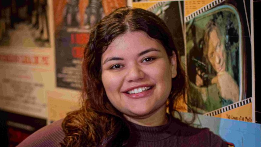 Mulher sorrindo em frente a cartazes de filmes, possivelmente em um cineclube.