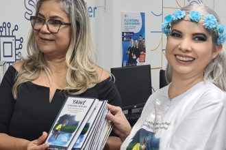 Mulheres sorrindo, segurando livros, em evento de distribuição literária para escolas.