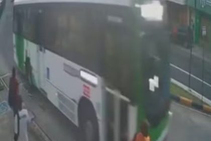 Ônibus branco e verde em movimento em via pública, com pessoas próximas e uma pessoa atropelada