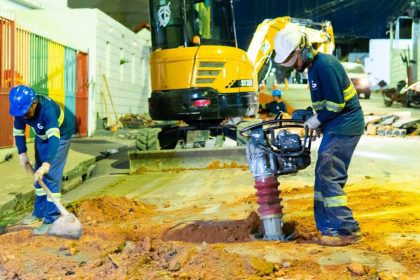 Operários trabalham em obras de saneamento em Manaus, utilizando máquinas e ferramentas.