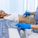 Paciente sorrindo durante exame de ultrassom abdominal com médico utilizando equipamento.