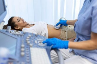 Paciente sorrindo durante exame de ultrassom abdominal com médico utilizando equipamento.