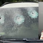 Para-brisa de carro com marcas de tiros e armas apreendidas.