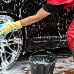 Pessoa lavando pneu de carro preto com esponja e sabão.