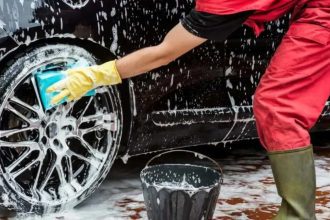 Pessoa lavando pneu de carro preto com esponja e sabão.