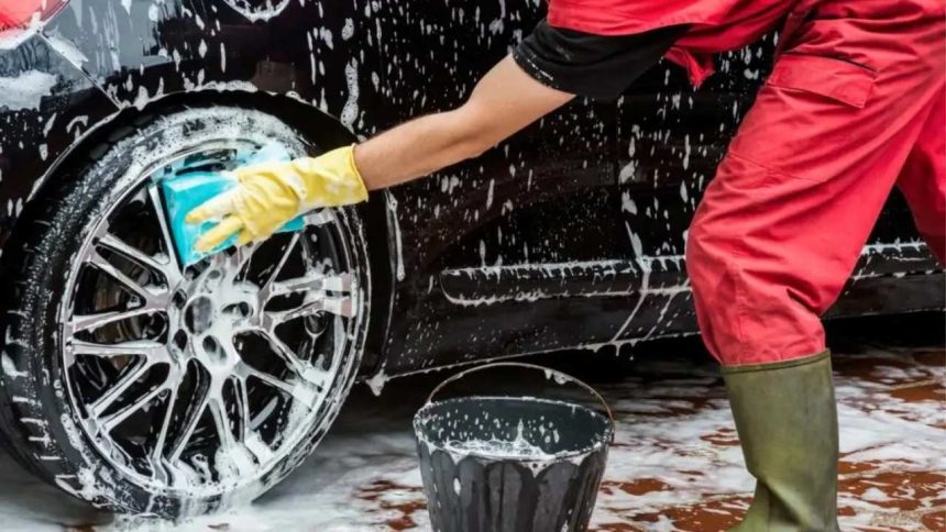 Pessoa lavando pneu de carro preto com esponja e sabão.