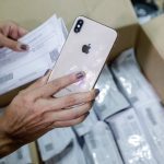 Pessoa segura iPhone e papel em caixa, possivelmente aparelhos apreendidos pela polícia em Manaus