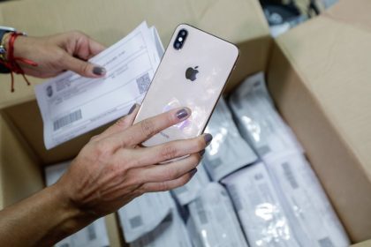 Pessoa segura iPhone e papel em caixa, possivelmente aparelhos apreendidos pela polícia em Manaus