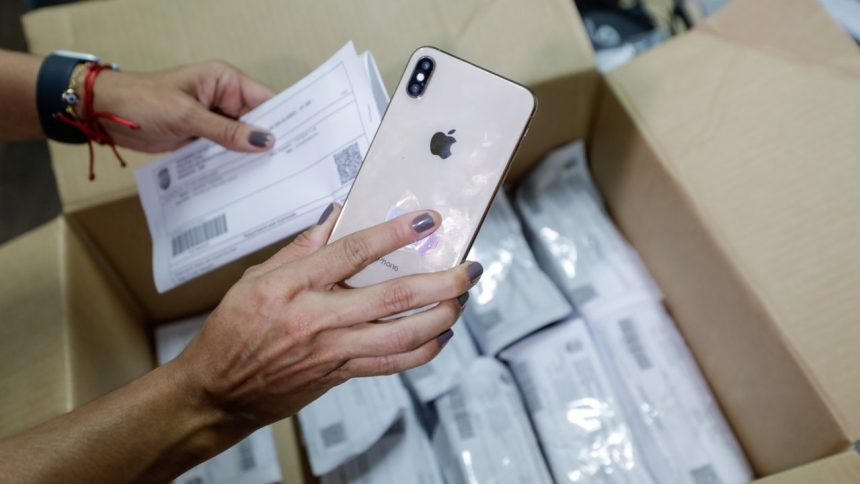 Pessoa segura iPhone e papel em caixa, possivelmente aparelhos apreendidos pela polícia em Manaus
