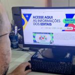 Pessoa usando computador com site de editais da Lei Aldir Blanc aberto, com informações sobre inscrições.