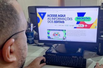 Pessoa usando computador com site de editais da Lei Aldir Blanc aberto, com informações sobre inscrições.