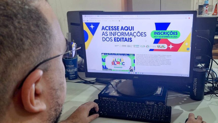 Pessoa usando computador com site de editais da Lei Aldir Blanc aberto, com informações sobre inscrições.