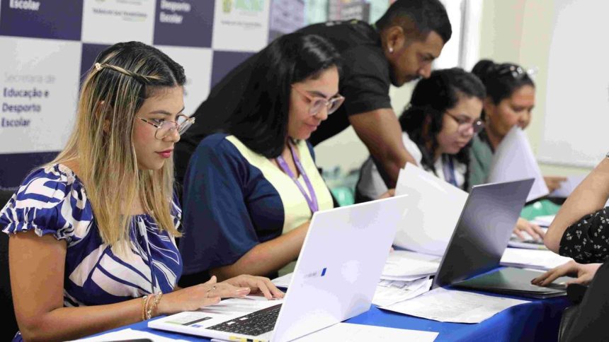 Pessoas em processo seletivo da Seduc preenchendo documentos e utilizando laptops.