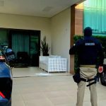 Policial em ação em frente a uma residência, possivelmente em operação contra crime organizado.