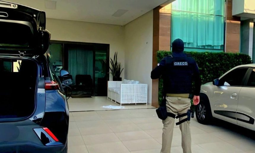 Policial em ação em frente a uma residência, possivelmente em operação contra crime organizado.