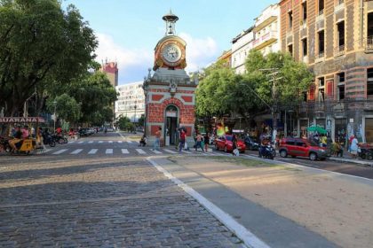 Praça com relógio de torre, carros e pessoas em Manaus.