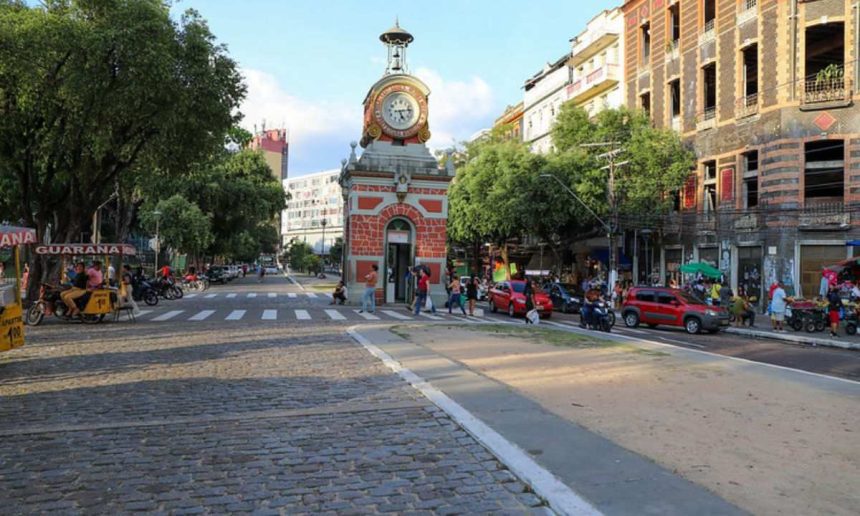 Praça com relógio de torre, carros e pessoas em Manaus.