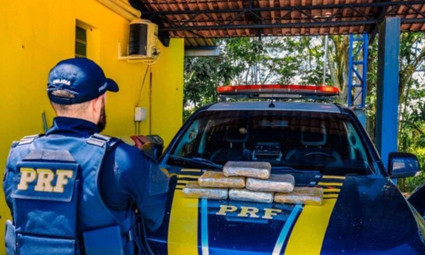 PRF apreende drogas em operação na BR-319. Policial em frente à viatura com drogas apreendidas.