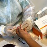 Profissional de saúde realizando teste rápido em paciente, usando luvas e jaleco.