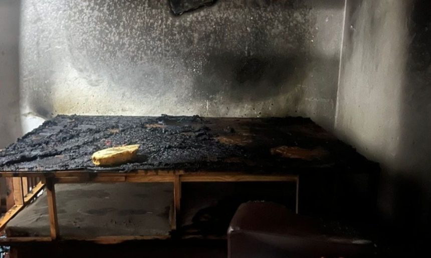 Quarto destruído por incêndio, com cama carbonizada e paredes enegrecidas.