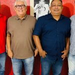 Quatro homens sorrindo, posando juntos. Um deles está com uma camisa vermelha para discutur o Carnaval 2026 de Manaus