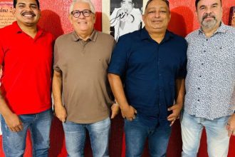 Quatro homens sorrindo, posando juntos. Um deles está com uma camisa vermelha para discutur o Carnaval 2026 de Manaus