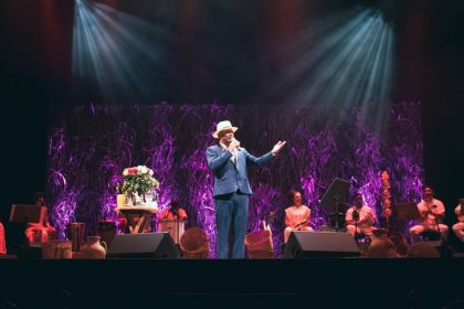 Show do cantor Antônio Bahia no Teatro ICBEU, com banda e cenário com flores.
