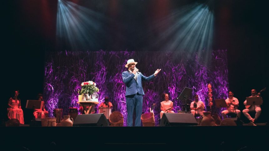 Show do cantor Antônio Bahia no Teatro ICBEU, com banda e cenário com flores.
