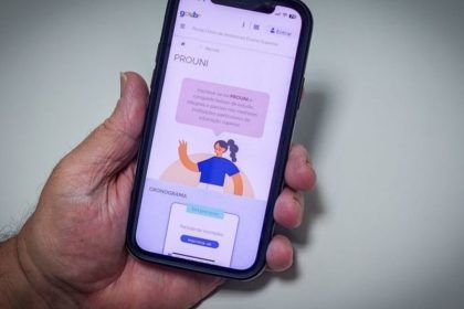 Smartphone com tela do PROUNI em primeiro plano, com detalhes sobre bolsas de estudo.