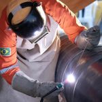 Soldador trabalhando em gasoduto em Manaus, usando equipamento de proteção.