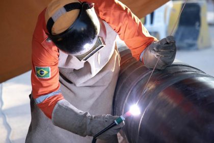 Soldador trabalhando em gasoduto em Manaus, usando equipamento de proteção.