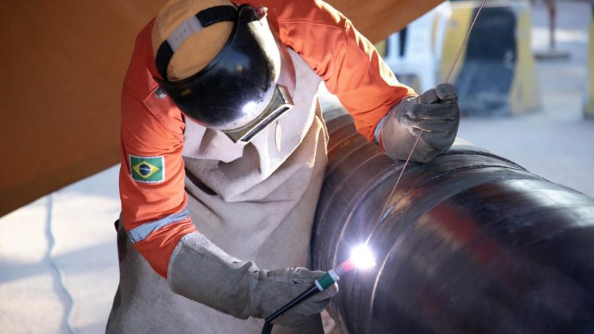 Soldador trabalhando em gasoduto em Manaus, usando equipamento de proteção.