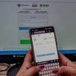 Telefone celular com a tela aberta em um site de saúde, com monitor de computador ao fundo