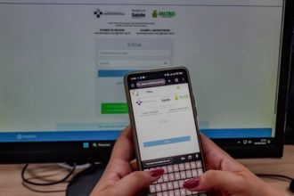 Telefone celular com a tela aberta em um site de saúde, com monitor de computador ao fundo