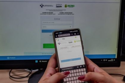 Telefone celular com a tela aberta em um site de saúde, com monitor de computador ao fundo