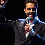 Thiago Arancam no palco, segurando um microfone e sorrindo.