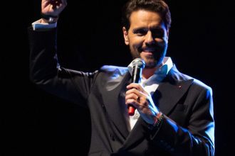 Thiago Arancam no palco, segurando um microfone e sorrindo.