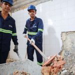 Trabalhadores da construção civil em ação, demolindo parede.