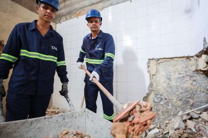 Trabalhadores da construção civil em ação, demolindo parede.