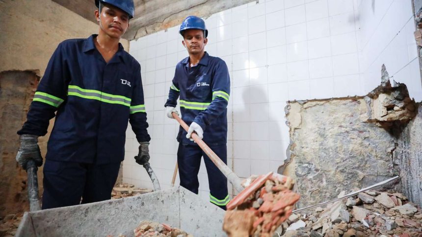 Trabalhadores da construção civil em ação, demolindo parede.
