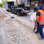 Trabalhadores em obra de infraestrutura urbana no centro de Manaus, com veículos de apoio.