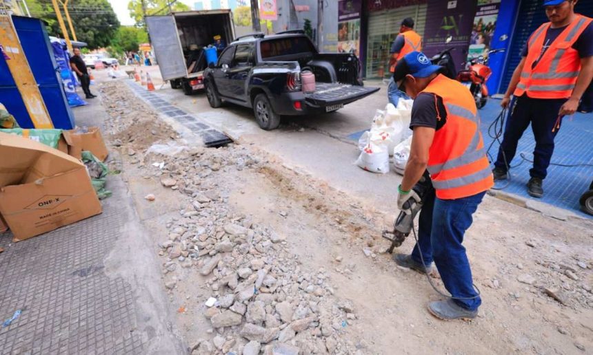 Trabalhadores em obra de infraestrutura urbana no centro de Manaus, com veículos de apoio.