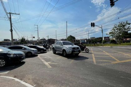 Trânsito na Avenida Silves com carros e motos, sob céu azul e sinalização.