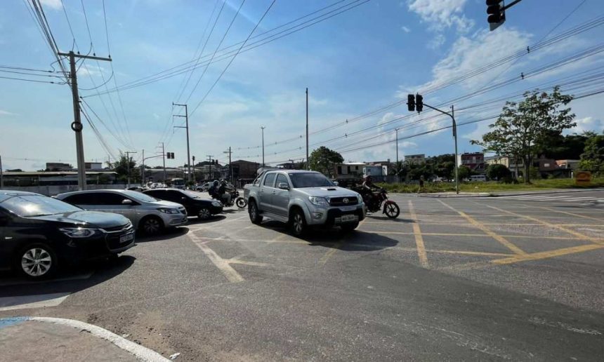 Trânsito na Avenida Silves com carros e motos, sob céu azul e sinalização.